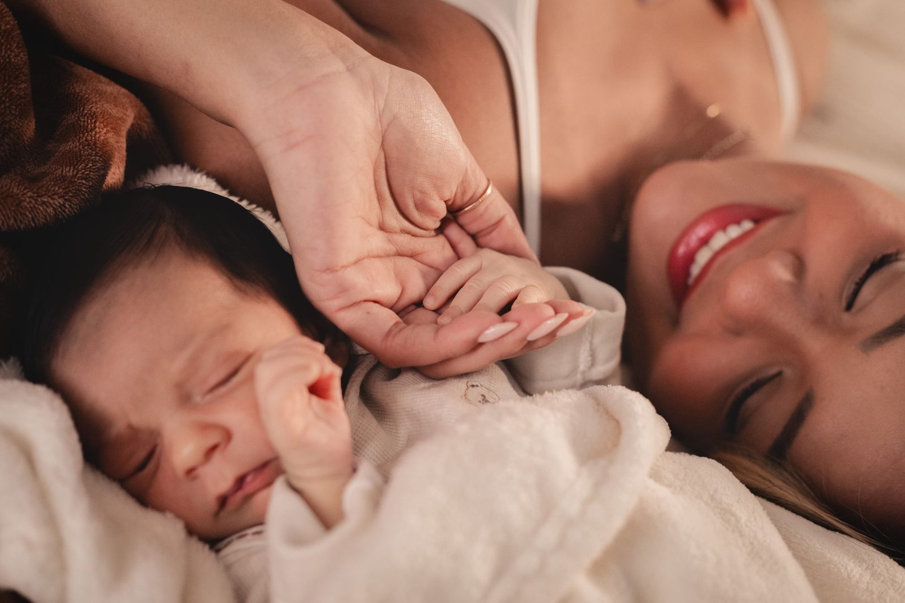 Newborn baby wrapped in a white cloth, with the smiling mother beside them