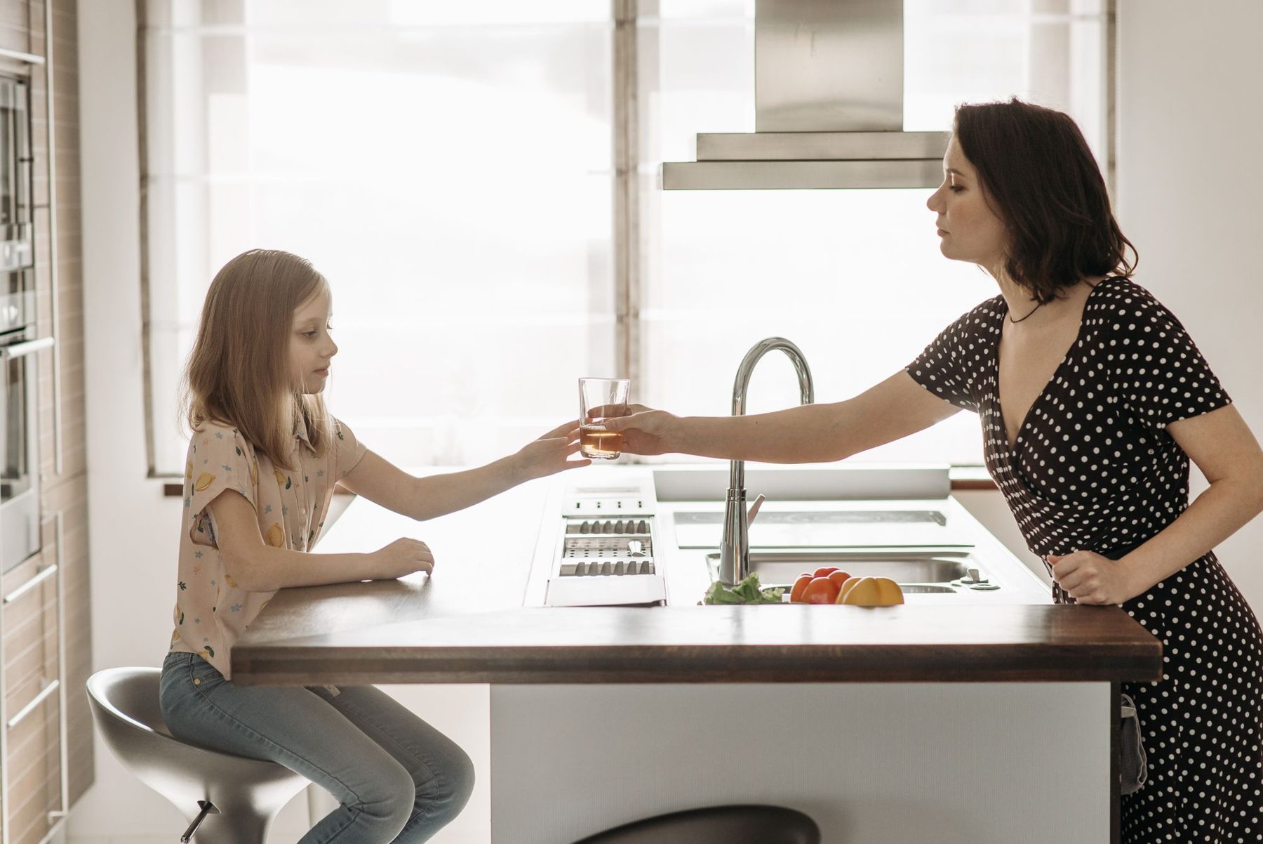 A mother hands her daughter a glass of water in the kitchen